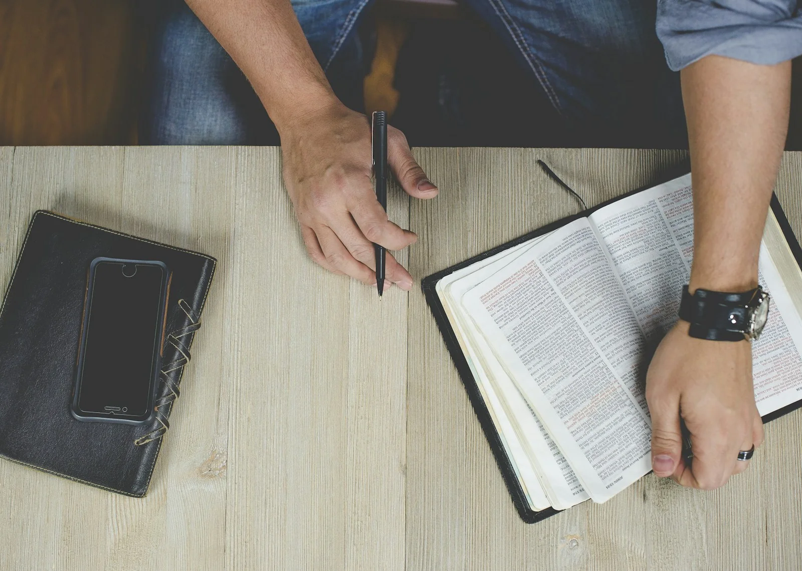 A person studying an open Bible with a pen at a wooden table